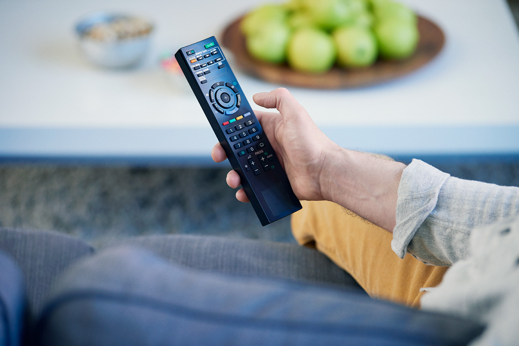 Henkilö istuu sohvalla ja pitelee kaukosäädintä kädessään